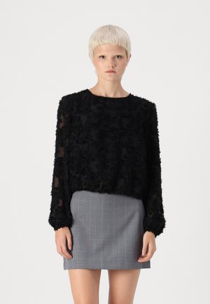 Black sheer top with textured floral pattern and long sleeves, paired with a gray checkered skirt. Simple round neckline.