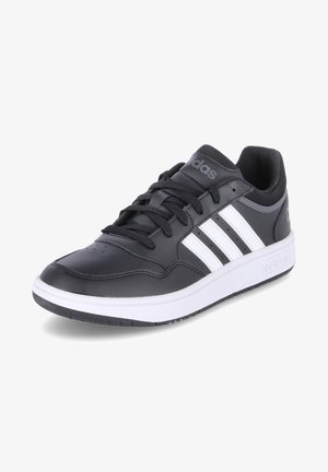 Zapatilla deportiva sintética negra con rayas blancas, puntera redonda, suela de goma plana y cordones en la parte superior. Presenta un cuello y una lengüeta acolchados para mayor comodidad.