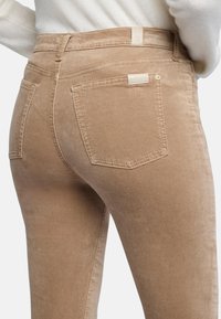 Bruine corduroy jeans met een soepele textuur, mid-rise pasvorm en achterzakken. Heeft een klein label op de tailleband en een knoopsluiting.