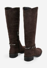 Botas altas de ante marrón, con tacón plano, cierre de cremallera y hebillas de acero en el tobillo. Textura suave y diseño minimalista.