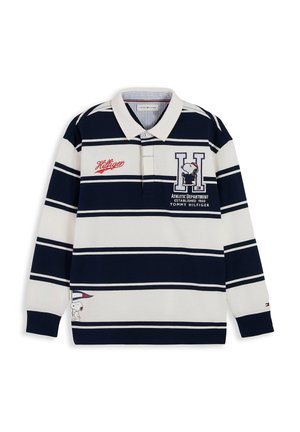 Smilende dreng iført en navyblå og hvidstribet langærmet polo med Snoopy og Tommy Hilfiger-logo, stående mod en hvid baggrund.