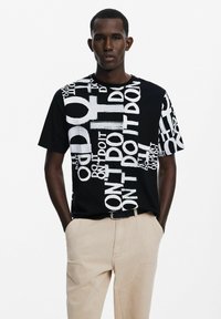 Camiseta de algodón negra con un gráfico en blanco de texto oversized que presenta "HAZ" y "NO HAGAS" en tamaños variables. Corte casual con mangas cortas.