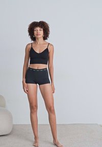 Soutien-gorge de sport noir avec des bretelles fines associé à un short noir. Tissu lisse, design ajusté et un détail de taille contrastant.