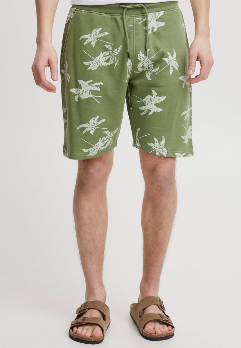Green beach shorts made of soft fabric, featuring white leaf patterns, an elastic waistband with a drawstring, and side pockets.