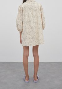 Kremsfärgad klänning med puffärmar och blommönster, med veck bak. Matchad med lavendelfärgade slip-on skor.