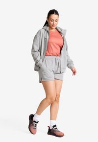 Ljusgrå zip-up hoodie, korallfärgad t-shirt och grå shorts; kombinerat med svarta och rosa athletic skor och vita strumpor.