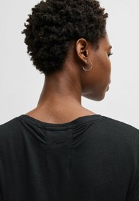 Top nero a maglia con vestibilità morbida, caratterizzato da un collo posteriore arricciato e un piccolo logo sul retro. Texture liscia e tessuto morbido.