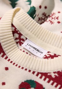 Crème gebreide trui met rode en groene kerstpatronen, voorzien van een ribbelkraag en een label met "Lindbergh White."