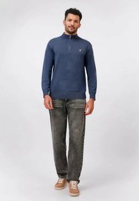 Navy zip-neck pullover made of cotton blend, paired with faded grey jeans and light-colored sneakers. Simple design, no patterns or accents.