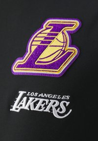 Svart idrottsklädsel med en broderad lila och gul Los Angeles Lakers-logotyp och vit text "Los Angeles Lakers".