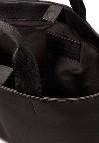 Czarna skórzana torba tote z materiałowymi uchwytami, posiadająca gładkie wnętrze i małą etykietę wewnętrzną. Zakrzywiony kształt z wzmocnionymi krawędziami.