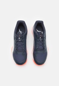 Baskets de sport marines avec un matériau en maille et synthétique, présentant des lacets noirs, un logo blanc et une semelle orange vif.