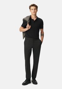 Zwarte polo, donkergrijze broek en zwarte schoenen. Grijs geblokte blazer over de schouder gedrapeerd. Eenvoudig ontwerp, getailleerde silhouette, textiel met textuur.