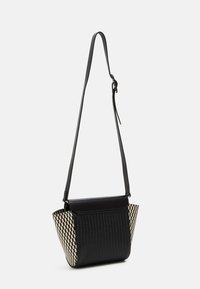 Mustekkaran ja beigein geometrijan kuvioinen laukku, jossa on jämäkkä muoto, kudottu tekstuuri ja säädettävä nahkahihna.