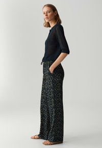 Pull en maille bleu marine à manches trois-quarts associé à un pantalon large à motifs dans des tons de vert foncé et beige, avec une taille à cordon.