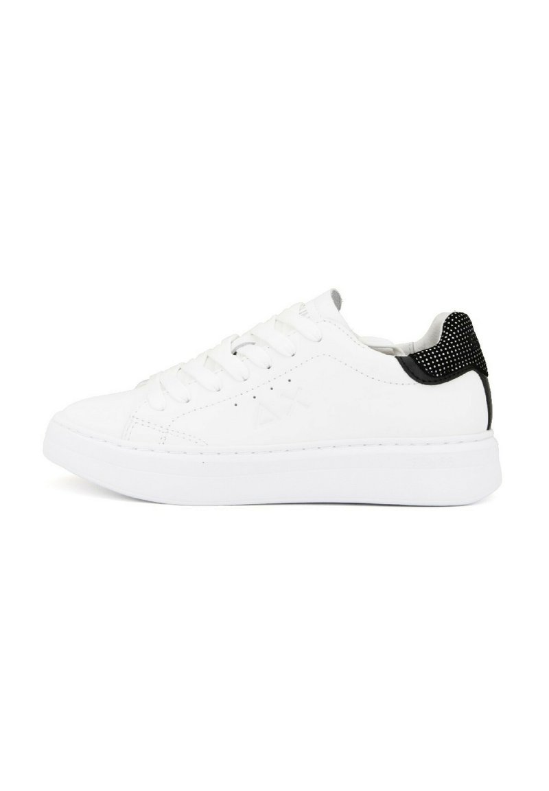 Zapatilla blanca con puntera redonda, parte superior de sintético suave, diseño de cordones y acento negro en la parte trasera con detalles texturizados.