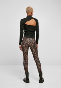 Svart langermet topp med et nøkkelhullsutsnitt bak, kombinert med tettsittende leopardmønstrede leggings og svarte kraftige ankelsko.