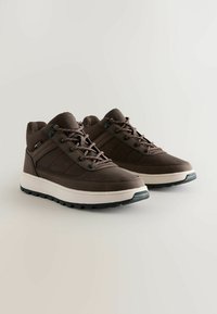 Ein Paar braune High-Top-Sneaker mit weißen Sohlen und schwarzem Profil, ausgestattet mit Schnürsenkeln und einem kleinen Stoffetikett an der Seite.
