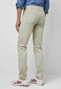 Beige slim-fit broek met vijf zakken, subtiele stiksels en een middelhoge taille, gecombineerd met witte sneakers met rode en blauwe accenten.