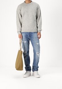 Szary dziany sweter, przetarte niebieskie dżinsy, białe trampki i beżowa torba. Zauważalne przetarcia na dżinsach i prążkowane mankiety swetra.