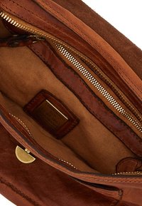 Interno in camoscio marrone di una borsa con dettagli in pelle liscia, chiusura con cerniera e etichetta in tono oro. Texture con una morbida fodera in tessuto.