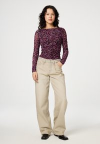 Langärmliges Oberteil aus schwarzem Mesh mit einem mehrfarbigen Blumenmuster, kombiniert mit beigen, hoch taillierten Schlagjeans und schwarzen Schuhen.