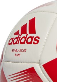 Balón de fútbol mini Adidas Starlancer, principalmente blanco con acentos rojos, presenta una superficie sintética suave y un diseño de logo distintivo.