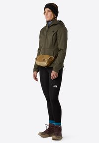 Olive green zip-up jacket, black leggings, brown hiking boots, light brown fanny pack; worn with a black headband and turquoise socks.
