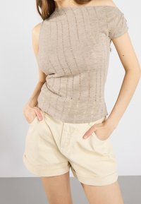 Beige off-shoulder toppi, jossa on teksturoidut raidat, yhdistettynä vaaleanvärisiin, käännettyihin shortseihin, joissa on sivutaskut. Molemmat vaatteet ovat kevyitä.
