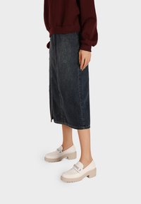 Zoccoli bianchi con una spessa suola beige, caratterizzati da un dettaglio con fibbia argento. Indossati con una gonna di jeans scura, abbinati a un maglione bordeaux.