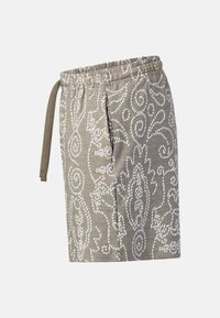 Short beige longueur genou avec motifs floraux et géométriques blancs complexes et taille élastique avec cordon sur fond uni.