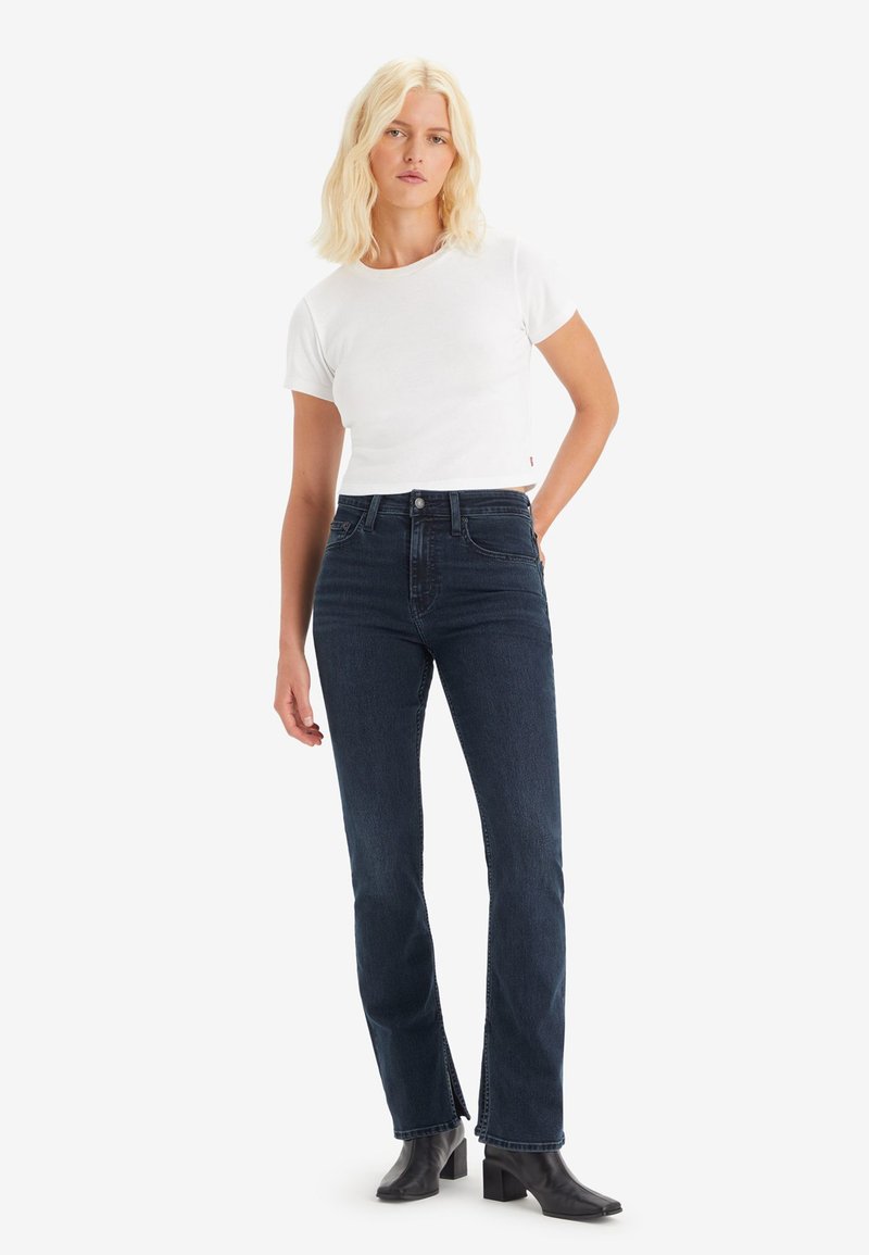 Högmidjade, mörkblå denimjeans med rak bendesign. Tillsammans med en vit, figurnära t-shirt med kort ärm och svarta klackstövlar.