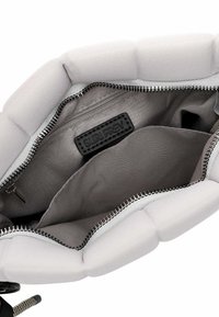 Interno della borsa in grigio chiaro con lati imbottiti, chiusura con zip, una tasca con zip e un'etichetta in tessuto con la scritta "SURI FREY." Tessuto liscio.