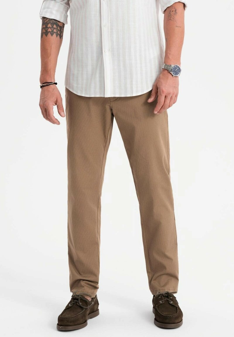 Pantalons en coton beige à coupe droite, avec une texture subtile, portés avec des chaussures en daim marron foncé et une chemise à boutons à rayures claires.