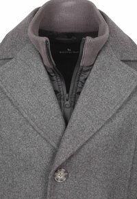 Grijze wollen mantelmix met een ontwerp in dubbele laag. Voorzien van een hoge kraag, ritssluiting en een knoopdetail aan de voorkant. Gladde, gestructureerde afwerking.