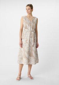 Beżowa kwiatowa sukienka midi z dekoltem w szpic, bez rękawów, z wcięciem w talii i zwiewnym dołem, w połączeniu z białymi sandałami na paski.