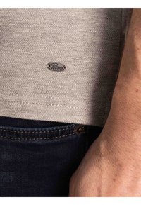 Grijze T-shirt van gestructureerde stof, met een klein metalen logo-label aan de zoom, gecombineerd met donkerblauwe denim jeans.