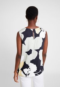 Blusa senza maniche con stampa floreale in verde chiaro, nero e giallo, dotata di una chiusura con spacco sul retro e realizzata in un tessuto morbido con una trama liscia.