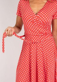 Rotes Wickelkleid mit weißen Punkten, aus glattem Stoff, mit kurzen Ärmeln und einem Bindegürtel in der Taille.