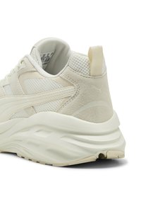 Scarpa sportiva beige realizzata in mesh e suede, con una forma arrotondata, dettagli testurizzati e un logo prominente sul tallone.