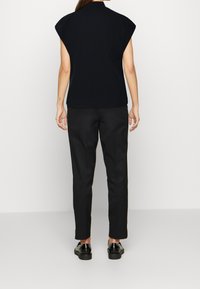Top nero a maniche corte con silhouette aderente, abbinato a pantaloni neri a gamba affusolata e scarpe nere. Tessuto liscio con un design pulito.