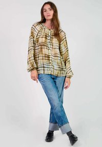 Gestreepte blouse met knopen in beige, bruin en teal, met poften mouwen. Gecombineerd met lichtblauwe jeans en zwarte schoenen.