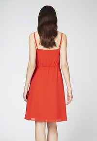 Rotes ärmelloses Kleid mit einem dehnbaren Bund, fließendem Rock und dünnen Trägern. Glattes Gewebe mit leichtem Material.