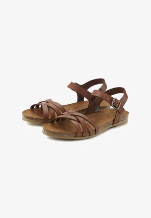 Sandali piatti in pelle marrone con cinturini incrociati e fibbia regolabile alla caviglia su suola in stile sughero.