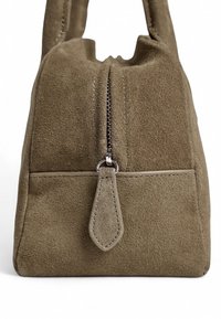 Sac en daim vert foncé de forme rectangulaire, avec une fermeture éclair sur le dessus, une anse plate, et une poche extérieure discrète avec un bord en couture.