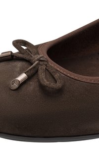 Κοντινή λήψη καφέ μπαλαρίνας από σουέτ με δεμένο φιόγκο και μεταλλικές άκρες στα κορδόνια, με στρογγυλεμένη μύτη και υφασμάτινη διακόσμηση.