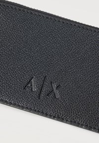 Δερμάτινη μαύρη ζώνη με υφή, ραμμένες άκρες και ανάγλυφο λογότυπο A/X σε λευκό φόντο.