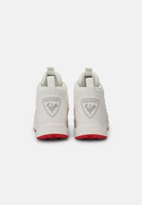 Sneakers alte bianche con logo grigio, suola rossa e linguette sul retro. Suola in gomma con grip testurizzato per supporto.