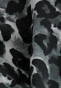 Material textil cu un model de imprimeu leopard în nuanțe de negru și gri, având o textură tricotată, care evidențiază diferite nuanțe de gri și accente negre.