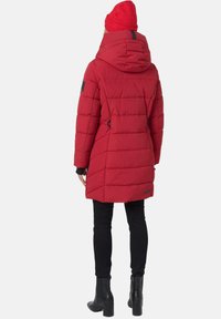 Red padded parka with a hood, featuring black accents and a textured design. Worn over black slim-fit pants and ankle boots.